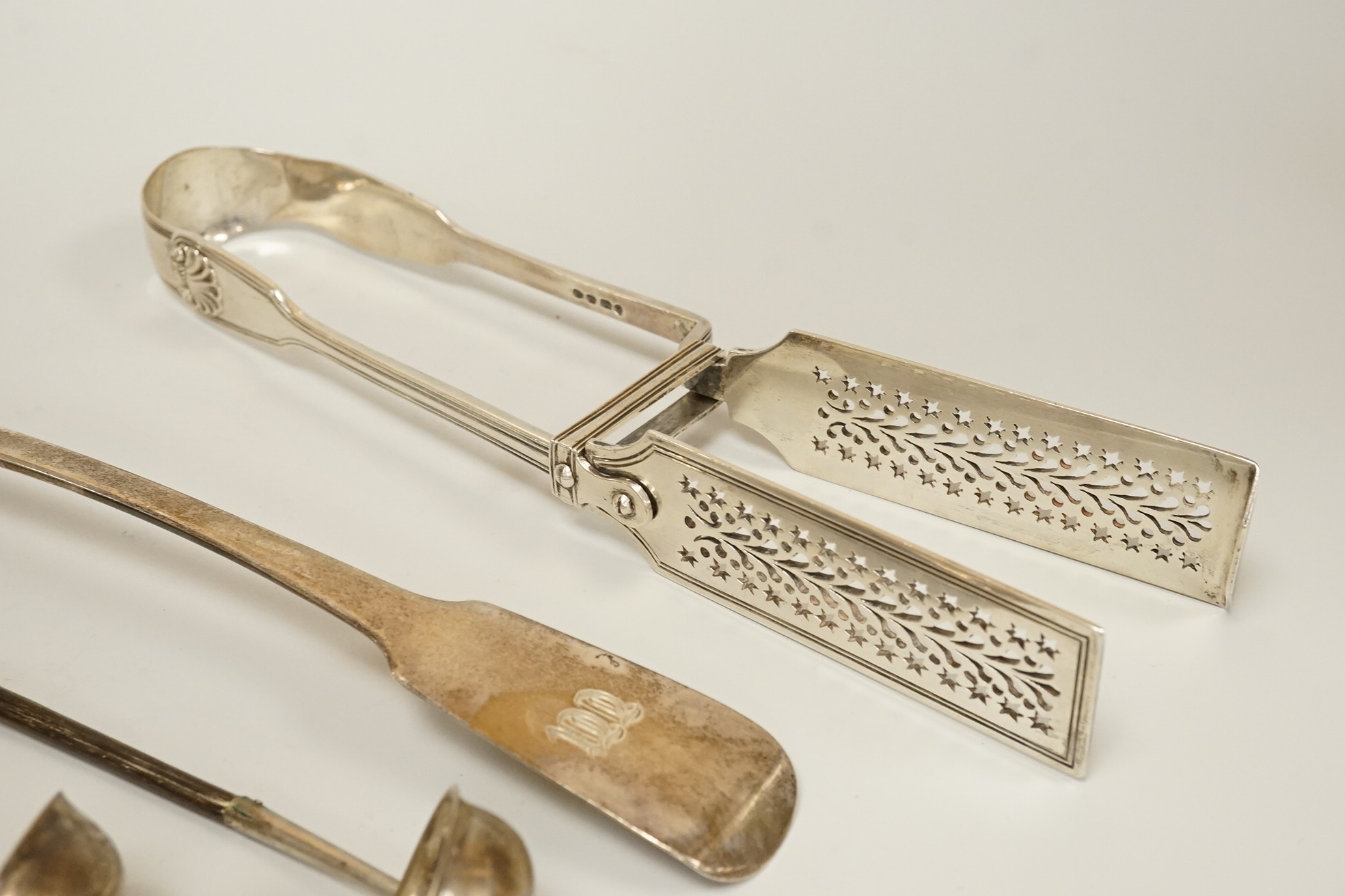 A pair of William IV silver fiddle, thread and shall pattern asparagus servers, a George IV silver fiddle pattern basting spoon, Robert Gainsford, Sheffield, 1826, 31.2cm, 10.8oz and two 19th century white metal toddy la